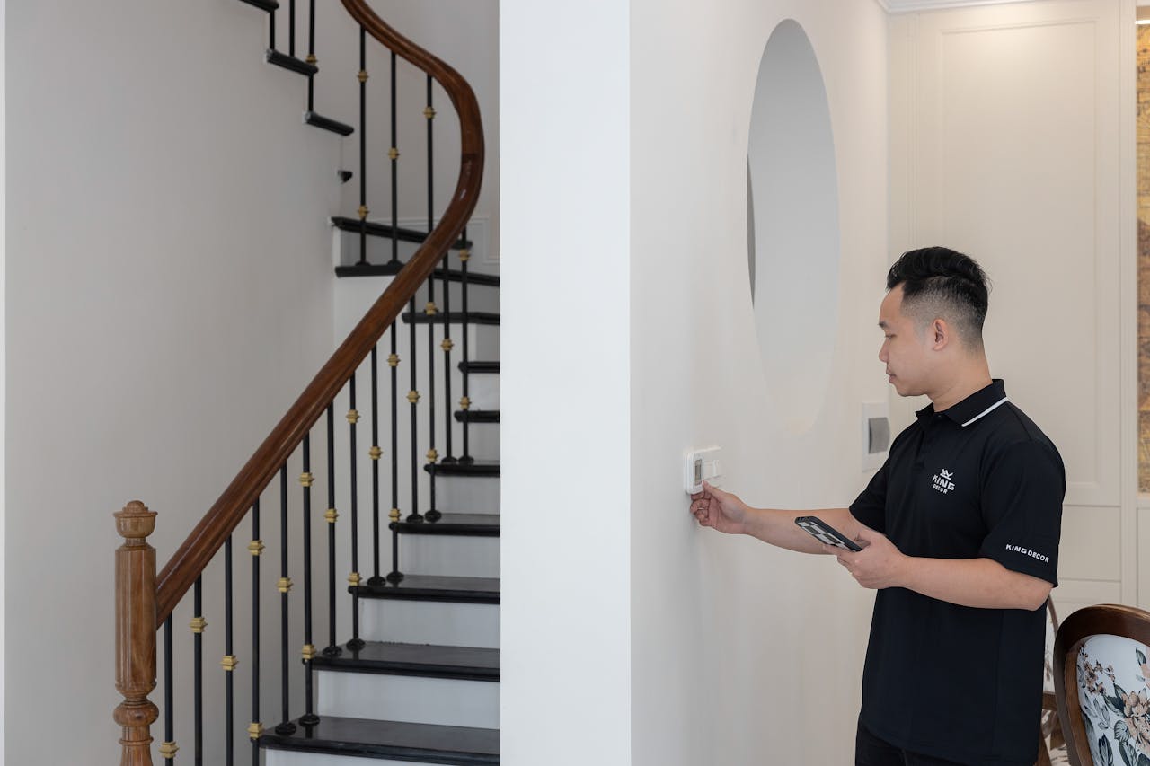 Man adjusting thermostat in stylish home with elegant staircase.